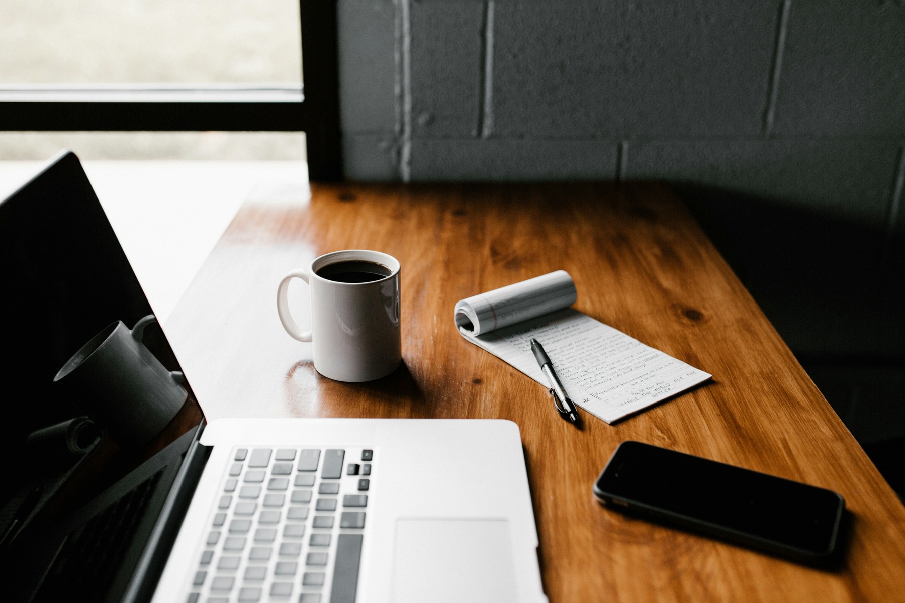 Wooden desk with laptop, notebook, coffee mug, and phone-calm workspace